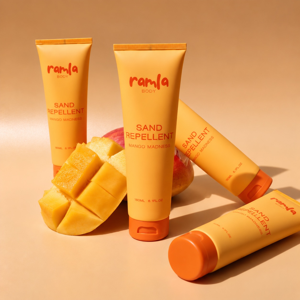 Four tubes of Ramla Body Sand Repellent in Mango Madness, arranged with fresh mango