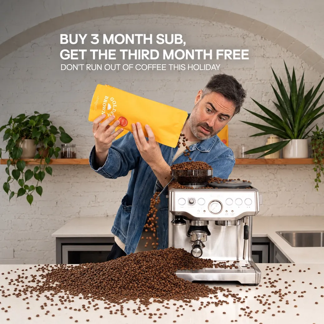 A Golden Brown holiday ad: a man in a denim jacket tips a yellow bag of beans into an espresso machine as they spill across the bench, under the offer Buy a 3 month sub, get the third month free